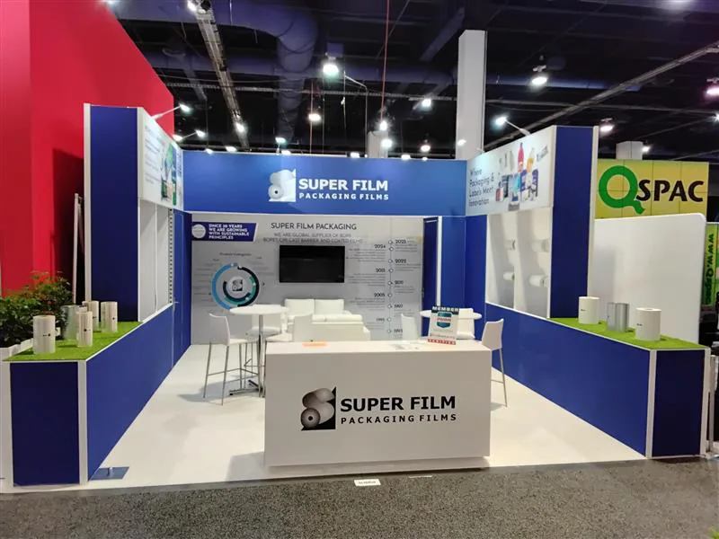 Blue-and-white island exhibit with open counters, lounge seating, and a central media wall.